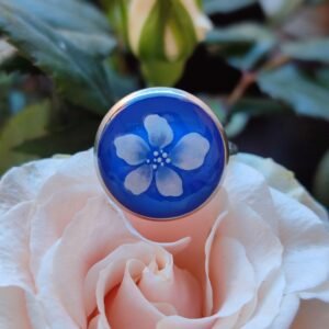 Anillo con base ajustable PLATEADA con UNA FLOR BLANCA (pegatina) encapsulada en resina.