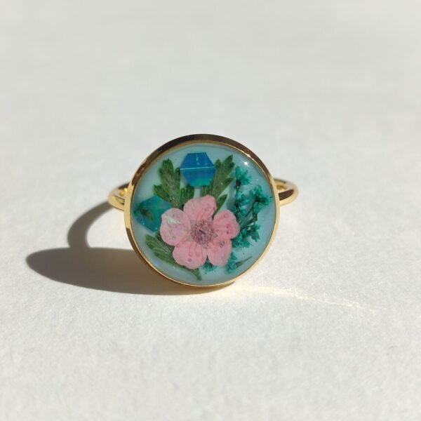 Anillo con UNA FLOR ROSA Y OTRA AZUL sobre fondo verde MENTA